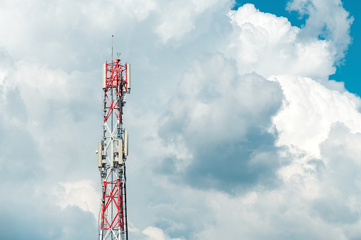Mobile telephony base station on communication tower against cloudy summer sky