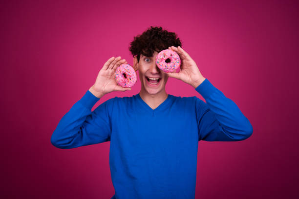 istock Young attractive guy eats pink donuts. Delicious breakfast and good vibes. 1600344501