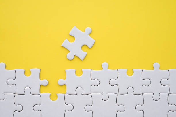 istock Unfinished white jigsaw puzzle on yellow background with copy space. Business strategy teamwork and problem solving concept. 1600345014