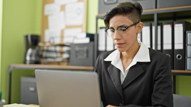 Young beautiful hispanic woman business worker using laptop taking glasses off at office