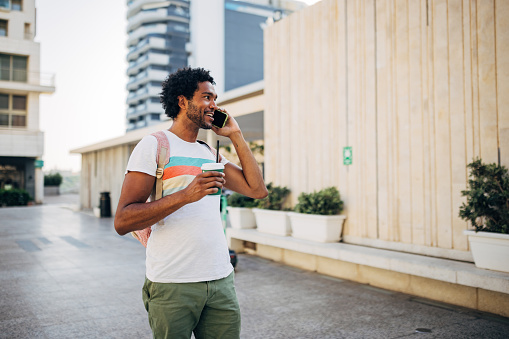 Carefree mixed race man makes a phone call while walking through the city alone enjoying the day