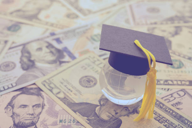 istock Graduation cap or hat on clear global earth with US dollars banknotes background. 1600389427