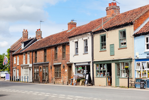 Row of shops, cottages and offices at Market Place, alongside the village green in the popular tourist location of Burnham Market in North Norfolk in East Anglia. The village has many Georgian style properties, some of which are stores, including bars, public houses, general stores, bookshops and galleries and cafes and tea rooms.