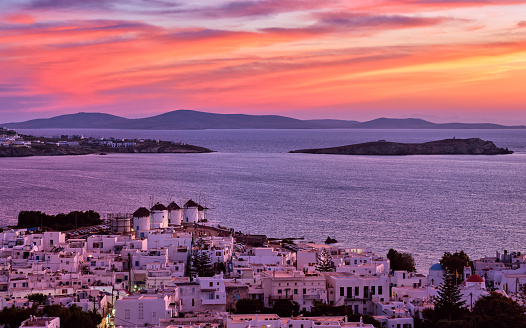 Beautiful sunset view of famous traditional white windmills on top of hill of Chora, Mykonos, Cyclades, Greece. Whitewashed houses, distant islands. Colorful sunset sky, hazy summer, iconic destination. Vacations, leisure, Mediterranean lifestyle
