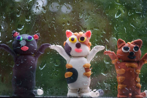Three colorful toy cats on the background of wet glass.