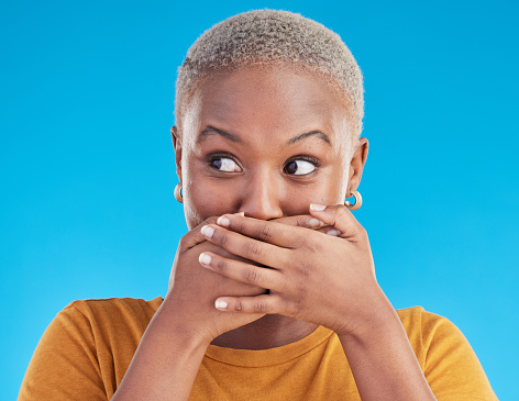 Gossip, wow or black woman shocked by secret, mistake or announcement in studio on blue background. Thinking, fake news or surprised girl with excited, wtf or omg expression with hands to cover mouth