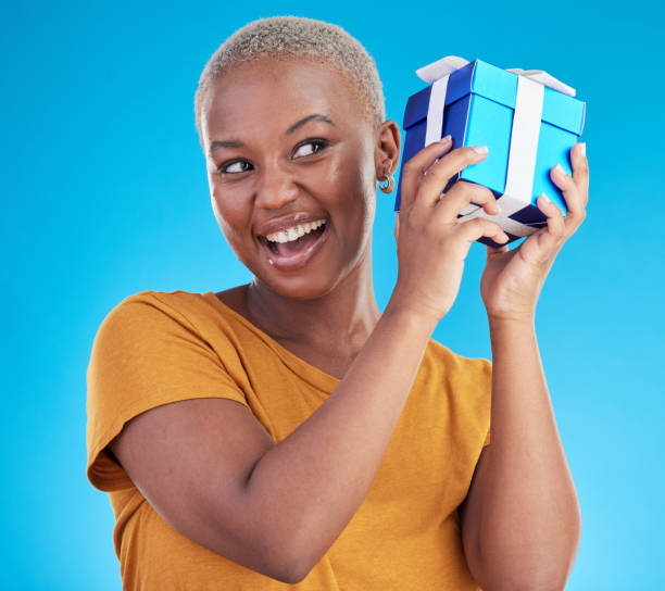 istock Shake gift, excited black woman with box and studio isolated on a blue background. Curious, happy and African person with present for party, celebration of holiday or birthday package for giveaway 1600507663