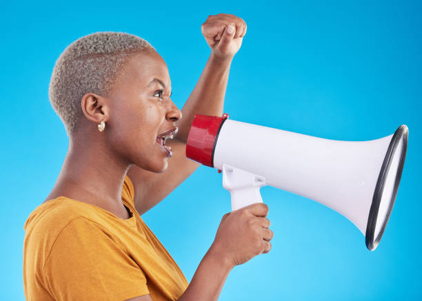 donna nera, megafono e protesta in studio, urla o profilo con pugno in aria per i diritti umani da sfondo blu. studentessa africana della generazione z, ragazza e tecnologia audio per il potere, l'opinione o l'annuncio di notizie - short phrase audio foto e immagini stock