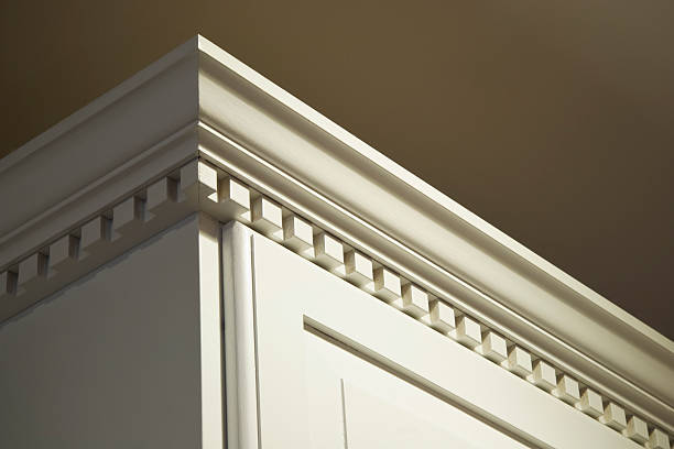 Solid Wood Kitchen Cabinet Crown Moulding Dentil Detail The top crown moulding dentil detail on some creme-color painted solid wood kitchen cabinets. These wall mounted cabinets do not go all the way to the ceiling above them. The lighting is coming from the top right from a ceiling light. moulding trim photos stock pictures, royalty-free photos & images