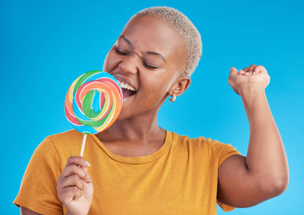 istock Lollipop, singing and a woman with candy in studio for sweets, rainbow and creative advertising. Happy black female person isolated on a blue background with sugar, freedom and happiness or color 1600521134