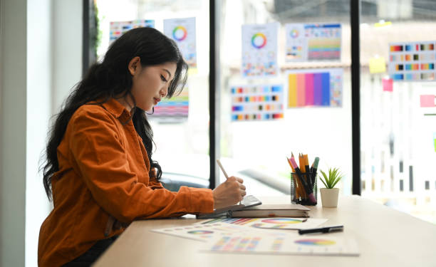 artista asiatica che disegna qualcosa su tablet digitale che lavora su un nuovo progetto di design presso un moderno ufficio creativo - fashion palette foto e immagini stock