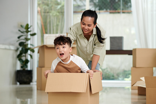 Mother pushing cardboard box with her son sitting inside