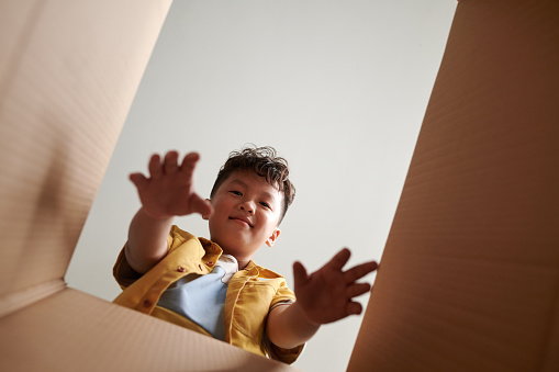 Smiling preteen boy taking toys out of cardboard box, view from inside