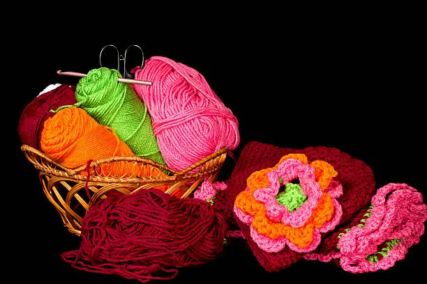 Basket of colorful and vivid colored yarns with project made out of them beside it.