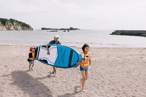 Japanese family works together to carry a sleek paddleboard, their coordinated efforts reflecting the bonds of love and togetherness.