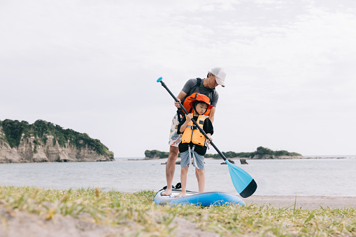 Japanese father and son engage in a paddleboarding lesson at the water's edge, their laughter and progress echoing the joy of learning by the sea.