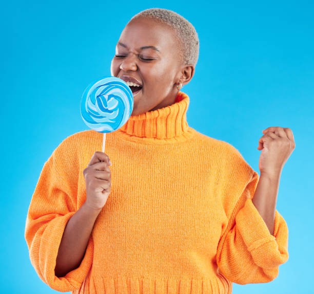 istock Singing, lollipop and a woman with candy in studio for sweets, rainbow and creative advertising. Happy black female person isolated on a blue background with sugar, freedom and happiness or color 1600566656