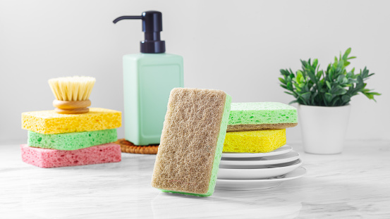 Sponges with white plates, dish washing and kitchen cleaning tools on marble table