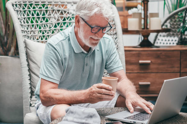 istock Senior bearded man sitting indoor using laptop typing on keyboard while surfing the net. Elderly white haired male enjoying tech and social 1600609093