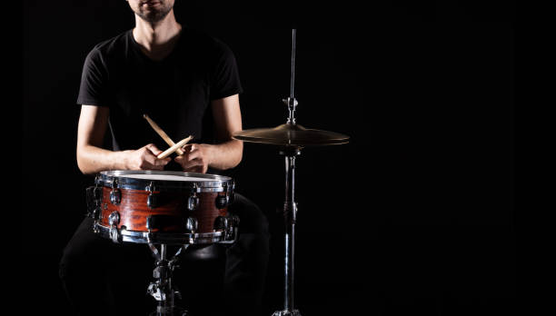 l'uomo suona uno strumento a percussione musicale con bastoncini da vicino su uno sfondo nero, un concetto musicale con il tamburo funzionante, bella illuminazione sul palco - samba dancing dancing drum drumstick foto e immagini stock