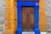 Old ottoman style ornate wooden door double in a bright blue painted stone frame set in a yellow wall in Rhodes Town, Greece