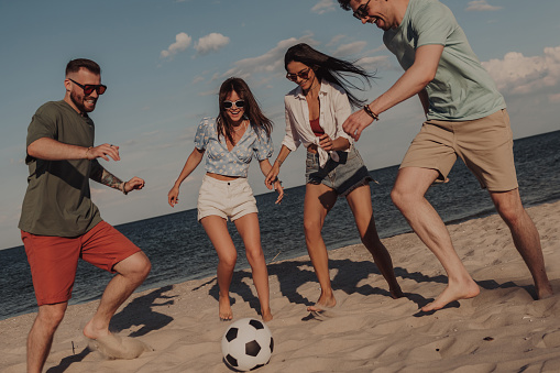 Group of happy friends spending fun time while playing soccer on the beach together