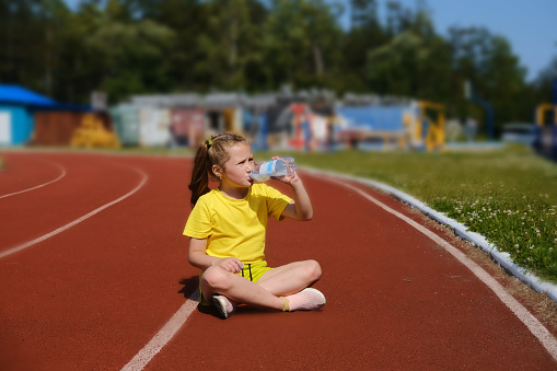 Fitness and sports. A girl is sitting on a treadmill at the stadium and drinking water after a workout.
