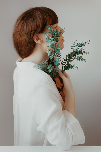 Redhead young woman profile portrait holding bouquet of eucalyptus leaves