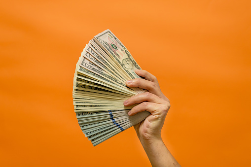 Man's hand holding currency money isolated on orange background