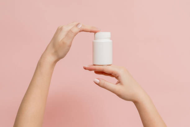 istock Plastic bottle (tube) in hands on pink background. Packaging for vitamins, tablets or capsule, or supplement 1600648988