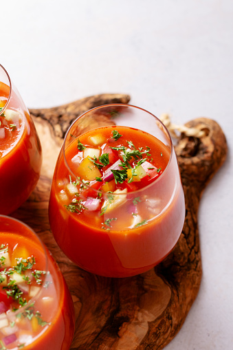 Spanish tomato gazpacho cold soup styled and decorated in glasses with ingredients on white table, top view