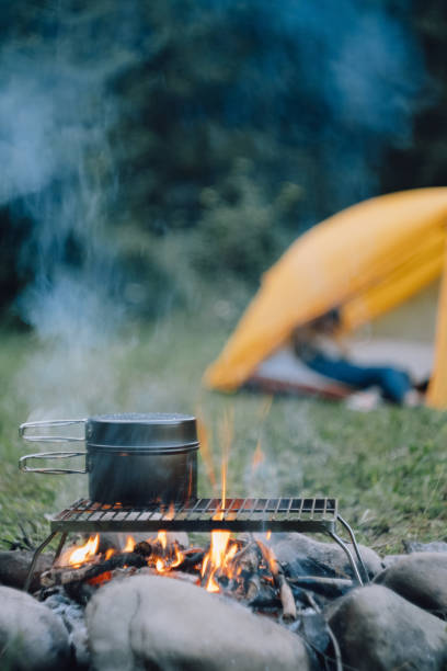 istock Cauldron over burning campfire with yellow tent on background green forest at warm evening. Bonfire cooking in summer or autumn season. Concept of adventure, travel and hiking. Fast dinner camping 1600659975