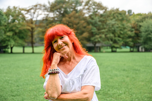 Portrait of a beautiful senior woman with long red or orange hair posing outdoors in a public park.