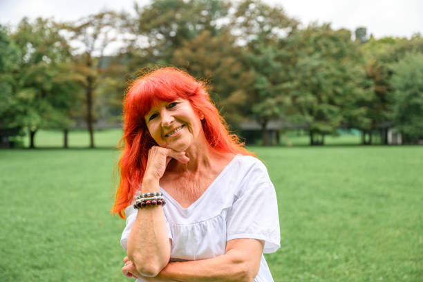 retrato de uma mulher sênior com longos cabelos vermelhos ao ar livre na natureza - cabelo pintado de vermelho - fotografias e filmes do acervo