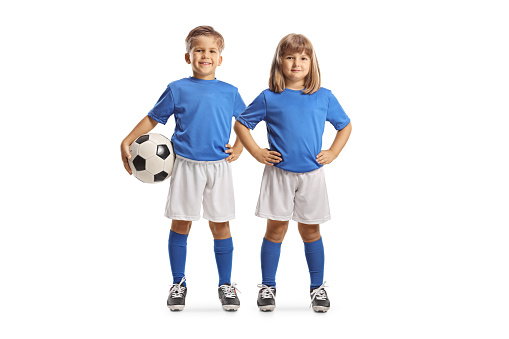Full length portrait of a girl and boy in a sports jerseys posing with a ball isolated on white background