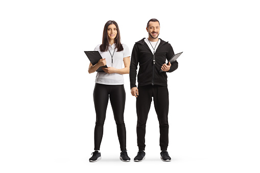 Full length portrait of a female and male sports coaches with clipboards isolated on white background