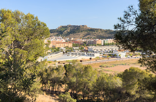 Buildings and houses in city, aerial view. Sagunto Castle on mountain. Ruins walls of Fortress Castle at town of Sagunto. Fortress Castillo in Mountains hills.  Houses roofs in town at mountains.