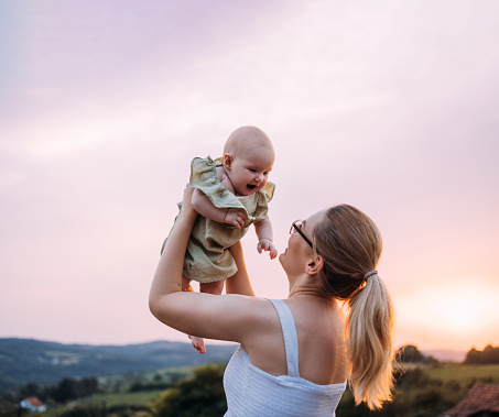 An anonymous woman standing in her backyard, holding her newborn baby up in the air.