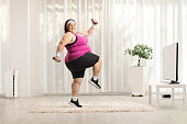 Overweight woman exercising with weights and smiling in front of tv