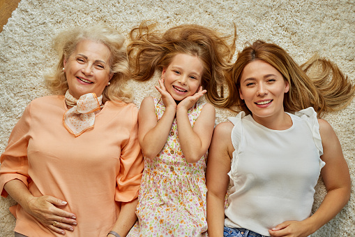 Mother, grandmother and granddaughter lying on carpet in the living room