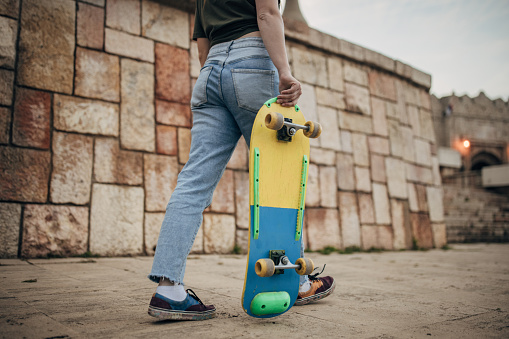 Modern young woman with skateboard outdoors in city.