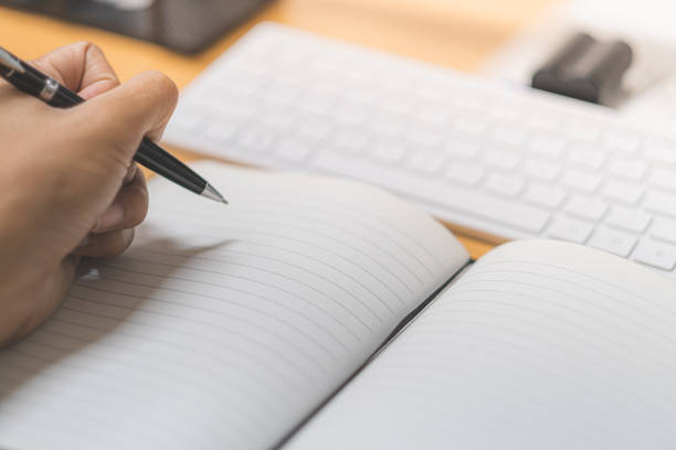 istock Close-up hand holding pen and write on white book 1600733802