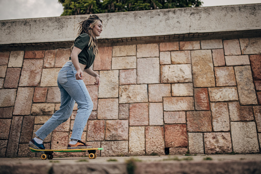 Modern young woman riding skateboard outdoors in city.
