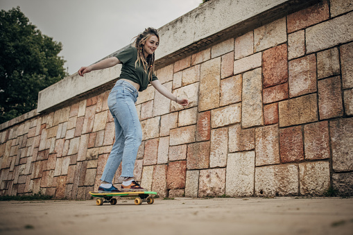 Modern young woman riding skateboard outdoors in city.