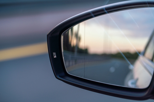 Side-view mirror close-up, riding at the multiple lane highway at sunset
