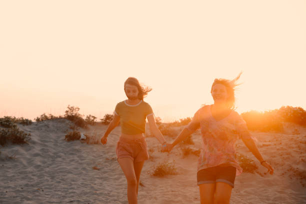 Mother and daughter running on the sand beach in sunset