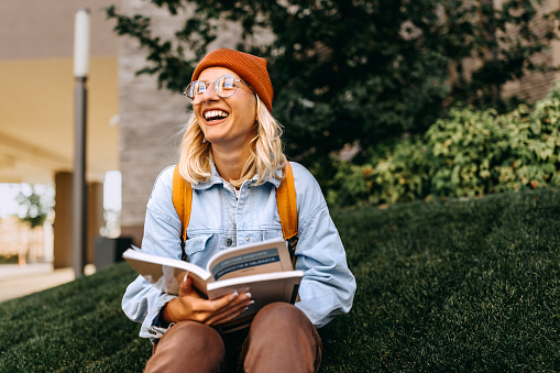 Young cheerful hipster woman studying outdoors in campus
