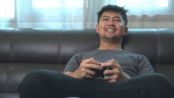istock Asian young man having fun playing video games sit sofa at home. 1600784016