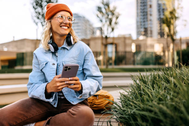 istock Young hipster woman using phone while sitting on the bench outdoors 1600784022