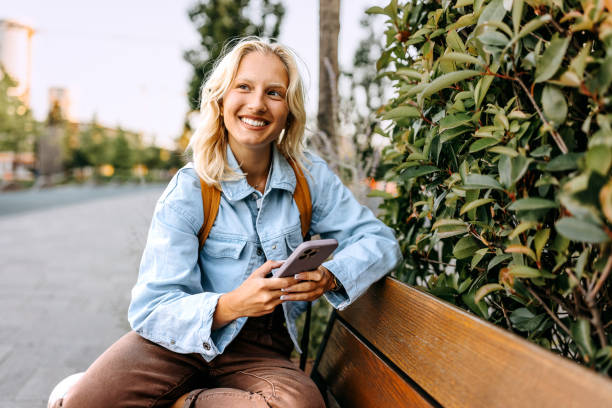 istock Young beautiful woman using phone while sitting on a bench 1600787336
